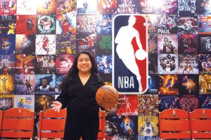 Paige Senal holding a basketball while standing in front of an NBA backdrop.
