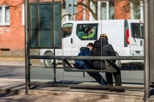 An adult and a child wait at a covered bus stop.