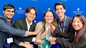The Biofide team poses for a photo, touching their trophy against a blue backdrop with the Johns Hopkins logo.