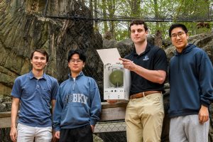 4 students stand outside a bobcat enclosure. One holds a prey node - a white box with sensors and a green sphere inside.