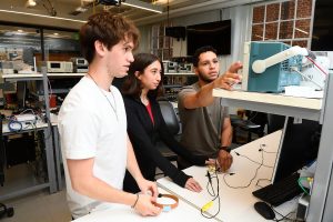 Three students look at an oscilloscopes in a lab.