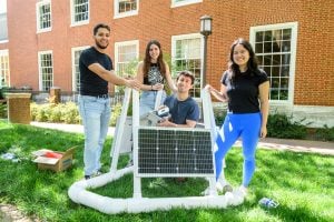 Four team members pose outdoors on campus with their oyster attraction device of solar panels and PVC pipe.