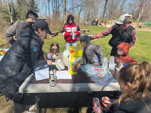 Students perform experiments at a table surrounded by kids and parents. 