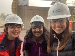 Two students and a TA outdoors wearing construction hats and goggles.