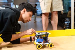 A student tweaks a small, wheeled robot on a simulated hockey surface.