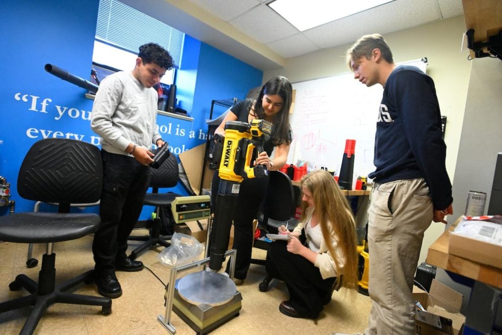 Four students stand around a leafblower while one holds it above an instrument. 
