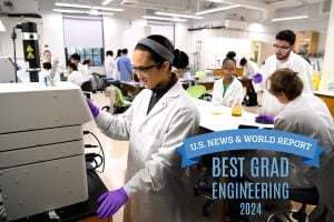 A student in a lab coat works on a lab machine in a classroom. Text is "U.S. News & World Report: Best Grad Engineering 2024."