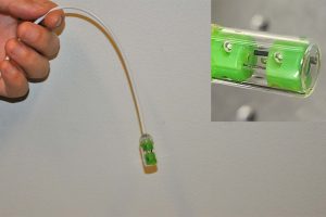 A hand holds a green capsule at the end of a tether. A close of the green capsule (inset)