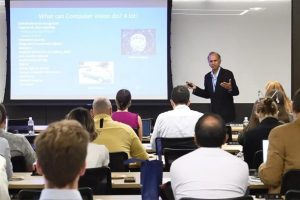 Rama Chellappa presents in front of a room full of seated attendees.