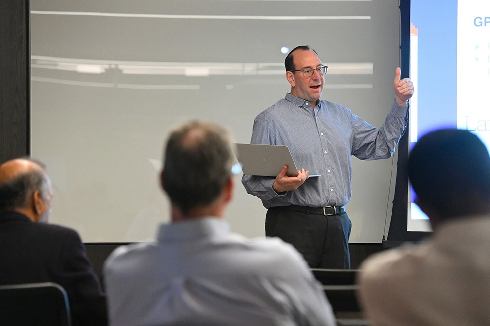 Mark Dredze presents in front of attendees, holding a laptop.