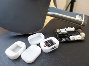 Photo of table tennis paddle and wireless sensors opened, exposing battery and other inner-workings.