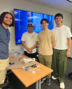 Photo of four PROPEL students smiling around a small, cardboard structure of a wagon.