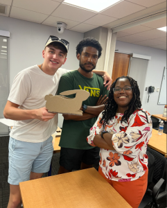 Photo of three students smiling and posing around a cardboard rabbit, pieced together by the students.