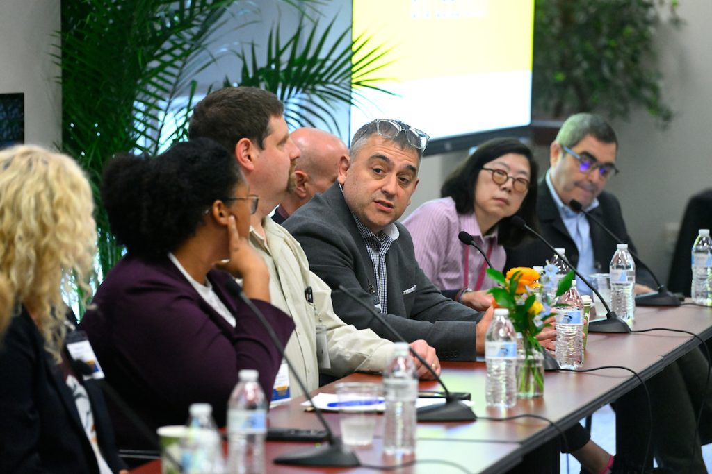 A group of panel members sitting at a long table. One panel member is speaking while others listen.