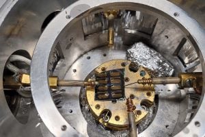 Interior view of a thermal evaporation chamber showing a circular metal mount with gold-plated components and wiring used for semiconductor device fabrication