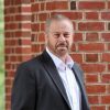 A photograph of Ed Schlesinger standing in front of a brick column