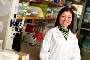 Jamie Spangler in a white lab coat poses for a photo in a lab setting