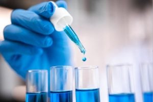 A gloved hand placing liquid into test tubes