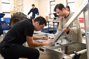 Sam Cohen and Charlie Margulies assemble a metal forklift design while Rachel Fox and David Hindman work on different components behind them.