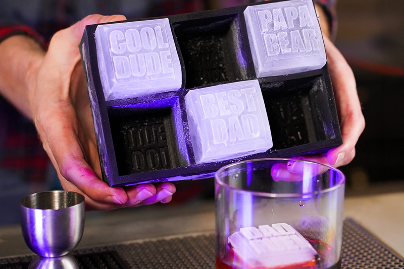 Hands hold a Silligrams ice cube tray with ice cubs that have "Best Dad," "Cool Dude" and "Papa Bear" engraved on them.