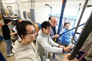 Thomas Gernay and team inspect a fire testing setup in a lab, observing structural components covered in insulation material.