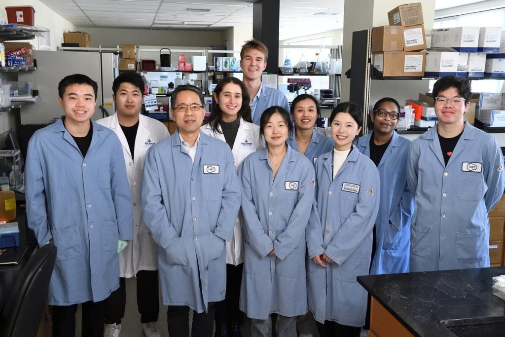 Professor Hai-Quan Mao poses with members of his research team in a lab setting, all wearing lab coats and smiling at the camera.