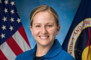 Official NASA photo of Rebecca Lawler in a blue NASA astronaut uniform. Behind her, an American Flag and NASA flag.