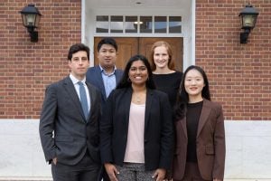 Four scholars pose on the steps in front of a campus building.