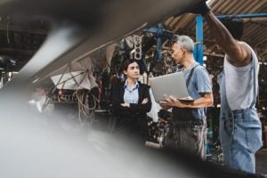 Professionals standing near machinery and discussing over a laptop