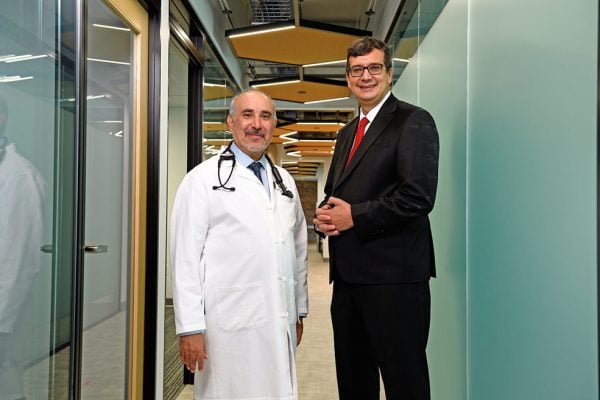 Peter Abadir (in a doctor's coat) and Najim Dehak (wearing a suit) in a modern-looking hallway. 