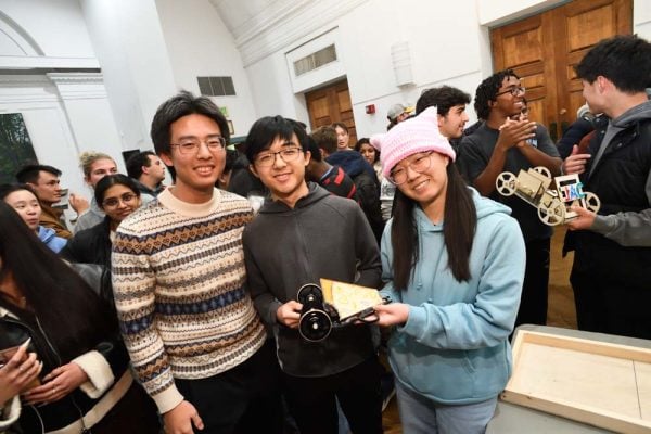 Three students smile while holding their award-winning “Pizza Car” entry at the JHU Freshman Design Competition.