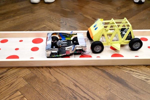Two creatively designed student-built cars collide head-to-head on the dotted wooden racetrack.