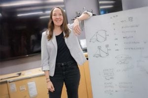 Photo of Alexis Battle standing with her arm propped onto a white board with written equations and figures