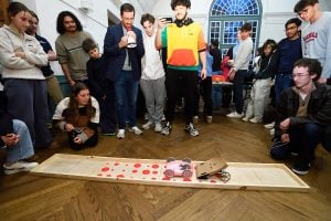 A packed crowd watches two cars battle on the track as an instructor calls the match.