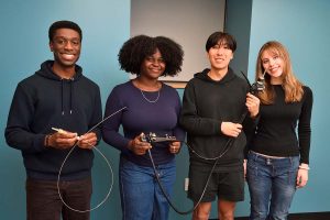 Four students holding an endoscopic device and needle components used in a multi-needle drug delivery system.