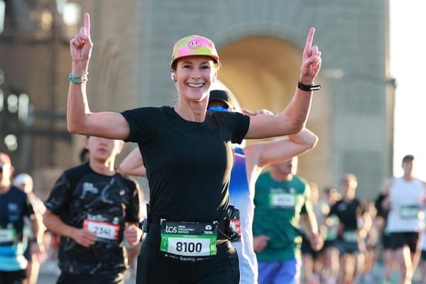 Alexis Dean raising her arms and smiles for the camera, as fellow marathoners run beside her. 