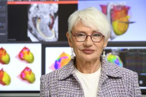 Natalia Trayanova poses for a photo in front of a variety of screens showing different visualizations of the heart digital twins.