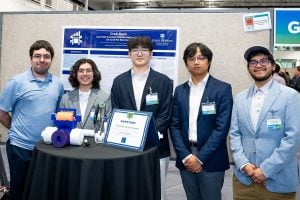The Crab-Back student team poses with their prototype and awards during Johns Hopkins Engineering Design Day, standing in front of their project poster and display table.