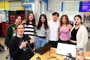 Biomedical engineering students pose together in a lab with their HypnosDx in-ear sleep monitoring device and testing setup.